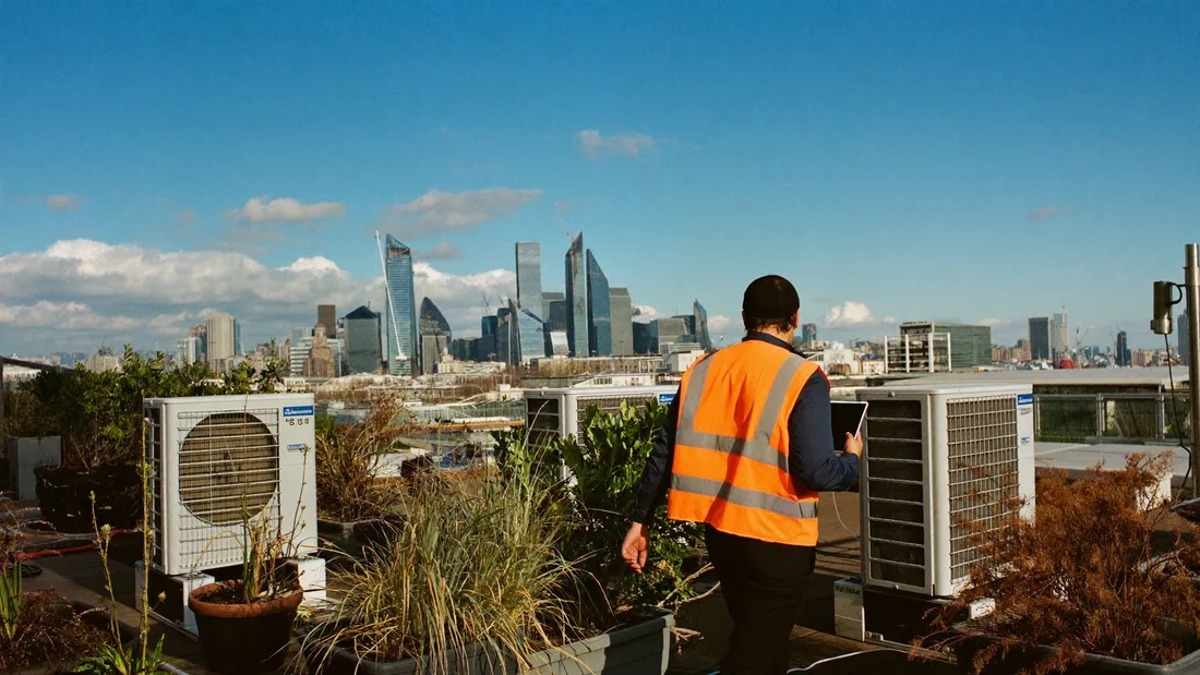 A technician crossing a rooftop plant deck on a bright morning, tablet in hand.